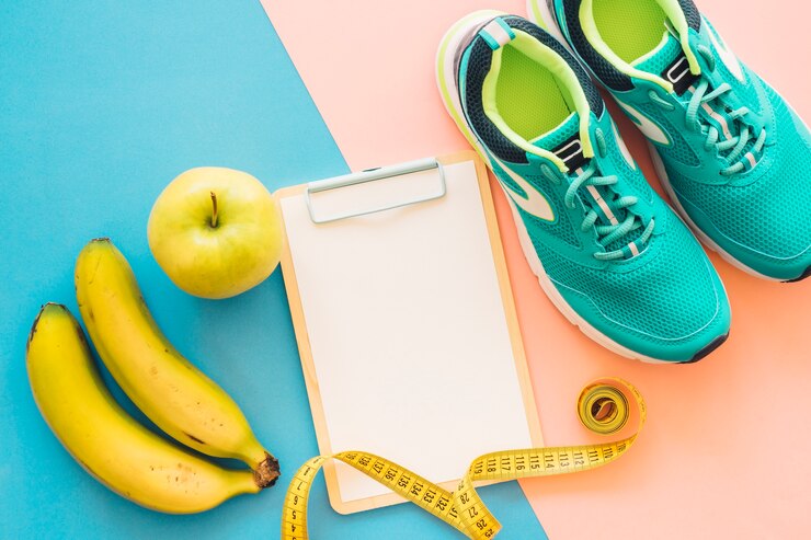 Sobre un piso se ve unas frutas, un centímetro, una pizarra y unas zapatillas deportivas celestes