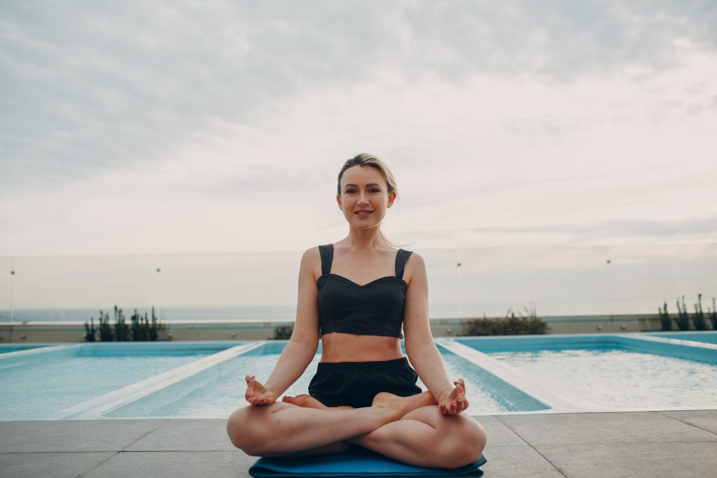 Una mujer con una leve sonrrisa, sentada sobre una colchoneta haciendo una posición de yoga.
