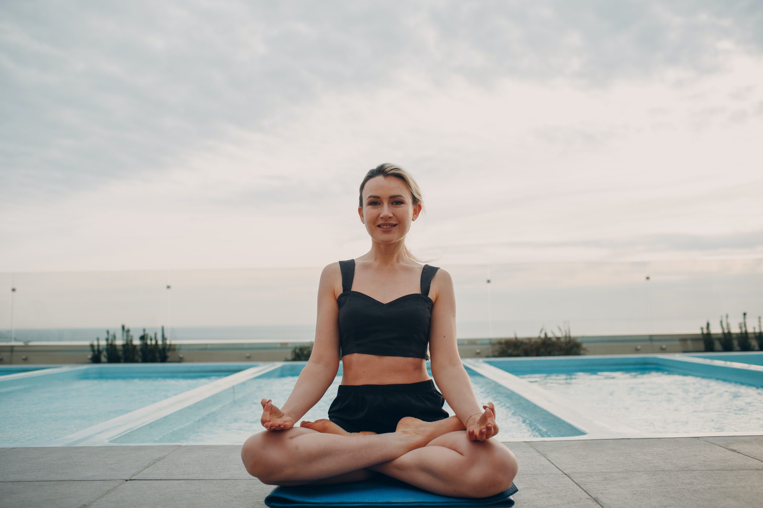 Una mujer con una leve sonrrisa, sentada sobre una colchoneta haciendo una posición de yoga.